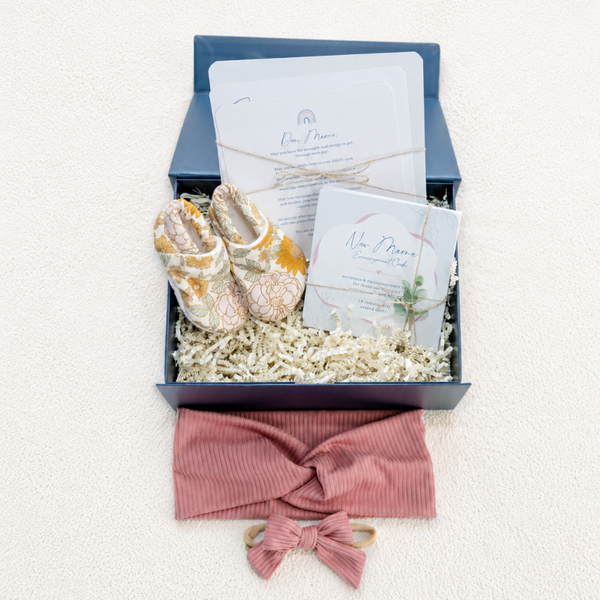 Gift box with baby shoes, headband, and papers on a white background