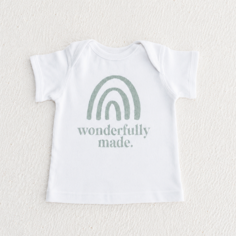 White baby onesie with green rainbow and text on a textured white background