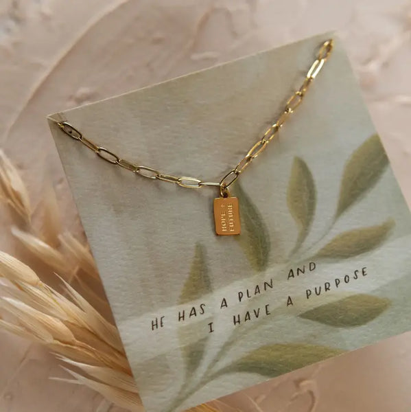 Gold necklace with paperclip chain and tag pendant that says "hope + future" on a card with verse Jeremiah 29:11